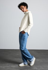 Hvid langærmet skjorte med krave, parret med løse blå jeans og hvide sneakers. Outfittet har en afslappet pasform.