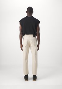 Top negro sin mangas y pantalones de color crema de corte recto, con una cintura alta y bolsillos traseros, vistos desde atrás. Calzado negro.