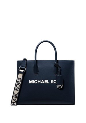 Navy blue Michael Kors tote bag with dual handles, a beige branded shoulder strap, and a small hanging MK logo charm.