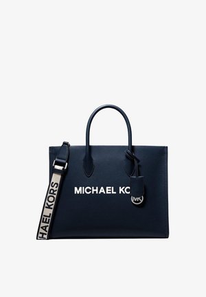 Bolso tote azul marino de Michael Kors con dos asas, una correa de hombro beige con marca y un pequeño colgante con el logo MK.