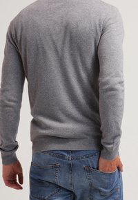 Pull gris en maille avec col rond, manches ajustées, et ourlet côtelé, porté sur un jean en denim bleu, montrant une texture douce et un design décontracté.