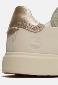 Sneaker con tomaia in pelle crema e accentuazione in metallo dorato sul tallone. Presenta logo impresso e suola in gomma testurizzata.