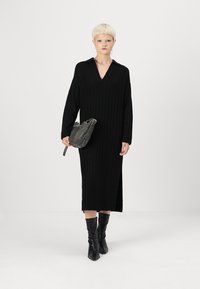 Mustmust väga hooajaline kleit V-kaelusega, pikkade varrukatega ja külglõigetega; komplekteeritud halli kotiga ja põlvepikkuste mustade saapadega.