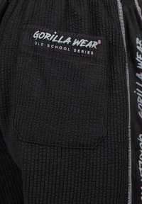 Zwarte, gestructureerde trainingbroek met een patch zak, voorzien van het logo "GORILLA WEAR OLD SCHOOL SERIES" in het wit en contrasterende zijstrepen.