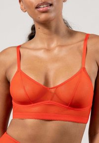 Orange bh i genomskinligt tyg med tunna band, med en triangulär kupa och en delikat vågig fåll.