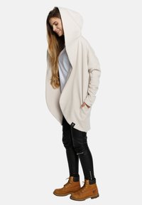 Kremowa, oversize'owa bluza z kapturem, luźny krój, długie rękawy i kieszenie boczne, w zestawieniu z czarnymi skórzanymi legginsami i brązowymi botkami.