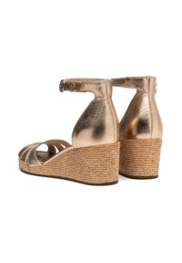Sandali wedge metallici dorati con piattaforma in juta intrecciata e cinturino alla caviglia. Il design open-toe presenta cinghie incrociate sulla parte superiore.