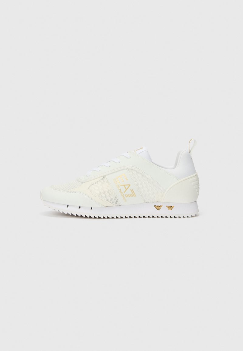 White athletic shoe with mesh panels, textured surface, and gold logo. Features a jagged rubber sole and heel tab for easy wear.