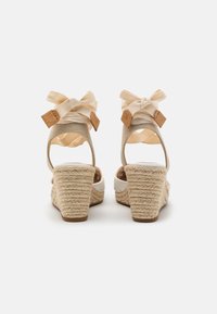 Klopné sandály s tkanou juteovou patou, béžovými plátěnými popruhy a stuhovými akcenty, které mají polstrovanou stélku a otevřený zadní design.