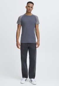 Gray and navy short-sleeve T-shirt with raglan sleeves, paired with black denim jeans and white sneakers, standing against a plain background.