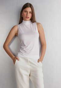 Witte, mouwloze coltrui gemaakt van een gladde, rekbare stof. Het ontwerp heeft een aansluitende silhouet en minimale details.