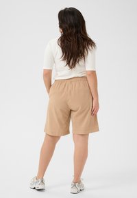 Tan, knee-length shorts made of lightweight fabric with an elastic waistband. Paired with white top and gray sneakers.