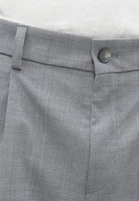 Calças cinzentas plissadas com uma textura suave, frente plana e fecho de um botão na cintura. Padrão de xadrez subtil visível.