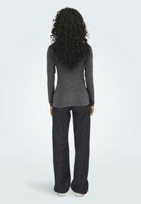 Gray long-sleeve top with a fitted design, paired with loose-fitting dark jeans and white sneakers. Hair is curly and falls to mid-back.