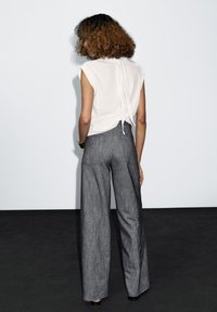 Light gray sleeveless top with a tie detail at the back paired with wide-leg dark gray trousers. Smooth fabric texture, casual fit.