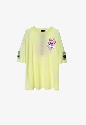 Camiseta amarilla de gran tamaño con cuello redondo, mangas cortas, gráficos de osos en la parte delantera y parches decorativos en las mangas.