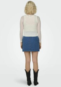 Un top alb cu mânecă lungă și textură ribbed, combinat cu o fustă mini din denim albastru și cizme negre de tip cowboy, prezentând o ținută casual stratificată văzută din spate.
