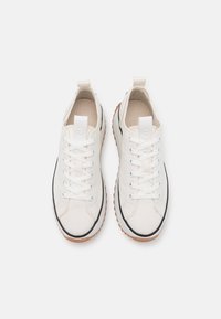 Sneaker di tela bianca con sei occhielli per i lacci, bordo nero sulla punta e suola in gomma. Presenta un piccolo etichetta bianca con logo sulla linguetta.