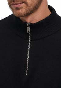 Schwarzer Pullover mit einem gerippten hohen Kragen und einem halb geöffneten Reißverschluss vorne. Besitzt eine glatte Textur und eine Metallreißverschlussdetail am Kragen.