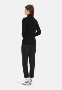 Schwarzer Rollkragenpullover, schlanker Schnitt, kombiniert mit dunklen Hosen und metallischen Stiefeletten. Glatte Textur mit minimalistischen Design.