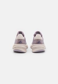 Zapatillas deportivas de color púrpura claro con parte superior de malla, acentos beige y una suela acolchada y texturizada. Presenta un logotipo de la marca en negro en el talón.