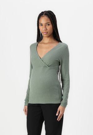 Maglione verde chiaro a maniche lunghe con scollo a V e texture a coste, design aderente, look a strati, abbinato a pantaloni neri.