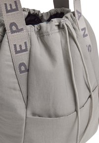 Borsa in tessuto grigio con parte superiore arricciata, caratterizzata da un esterno texturizzato, cordino regolabile e spallacci larghi con testo stampato.