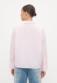 Light pink long-sleeve shirt with a textured fabric. Features sheer sleeves with small dots, classic collar, and buttoned cuffs.