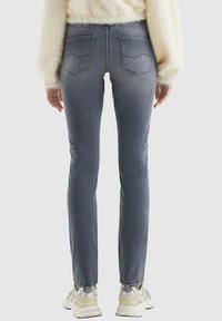Figurbetonte, dunkelgraue Jeans aus Denim mit Fünf-Taschen-Design, dezenten Stickdetails und ausgefranster Säume. Getragen mit hellen Sneakers.