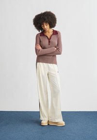 Top de manga comprida canelado, cor bordô com gola contrastante, combinado com calças largas brancas com riscas laterais. Sapatos plataforma grossos bege.