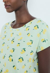 Πράσινο κοντομάνικο πουκάμισο με σχέδια από λεμόνια και λάιμ, που περιλαμβάνουν ολόκληρα και κομμένα φρούτα με πράσινα φύλλα, φτιαγμένο από μαλακό ύφασμα.