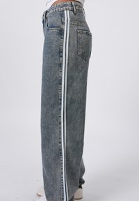 Light blue denim wide-leg jeans with white side stripes, high waist, and a single back pocket, featuring a textured finish.