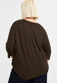 Ribbed pitkähihaine ruskea paita rentoa leikkuuta, leveä kaula-aukko ja pehmeä kangas, yhdistettynä tummansinihin farkkuihin. Takakuvassa näkyy hihojen pituus.