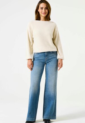 Cream, fluffy sweater with long sleeves paired with light-wash, wide-leg jeans. The outfit features minimal stitching and classic denim accents.