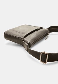 Černá kožená crossbody taška s nastavitelným textilním popruhem, která má hlavní přihrádku na zip a přední kapsu na klopu. Hladký povrch.