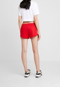 Pantaloni sportivi rossi con cintura elastica e spacchi laterali, abbinati a una maglietta bianca corta e scarpe da ginnastica nere e bianche.