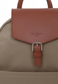 Zaino in tessuto beige con patta in pelle marrone, fibbia in argento e logo in rilievo. Texture liscia con un design minimalista.