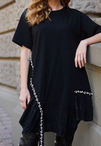 Czarna oversize sukienka z krótkim rękawem, z plisowanym dołem i dekoracyjnymi perłowymi akcentami z jednej strony. Gładka tekstura.