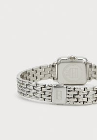 Silberne Edelstahl-Uhr mit quadratischem Gehäuse, Gliederarmband und graviertem Verschluss. Verfügt über ein minimalistisch gestaltetes Design und eine glatte Textur.
