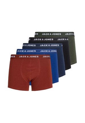 Mladý muž s krátkymi blond vlasmi oblečený v hnedých boxerkách Jack & Jones stojaci pred jednoduchým svetlým pozadím.