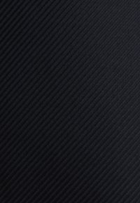 Gros plan d’un tissu noir avec une texture côtelée diagonale et un motif chevrons subtil.