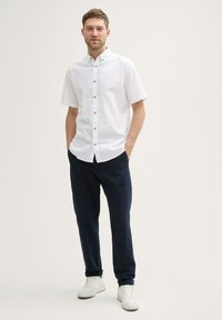 Chemise blanche à manches courtes avec de petits pois multicolores, col boutonné, associée à un pantalon navy et des baskets blanches. Design simple et décontracté.
