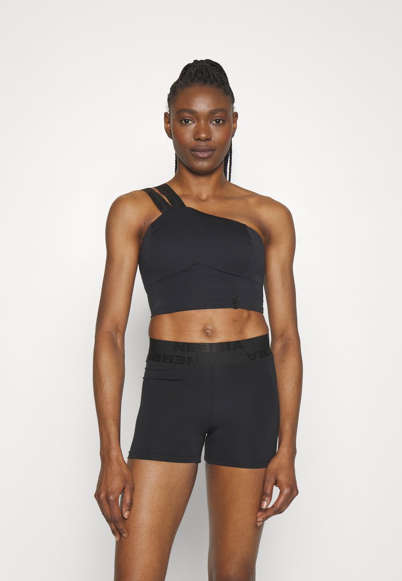 Crni atletski crop top s dizajnom na jedno rame i teksturiranim trakama, u kombinaciji s crnim uskim šortsevima koji imaju brendiranu gumicu.