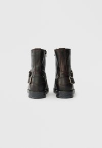 Rudos odinės kulkšninių botai su tekstūruotu paviršiumi, turintys šoninius užtrauktukus ir dekoratyvinius sagtis išorinėse pusėse. Juodi gumos padai.