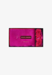 Funda de almohada de seda rosa con ribete naranja y texto dorado, acompañada de una coleta de seda con rayas rosa y naranja, presentada en una caja negra.