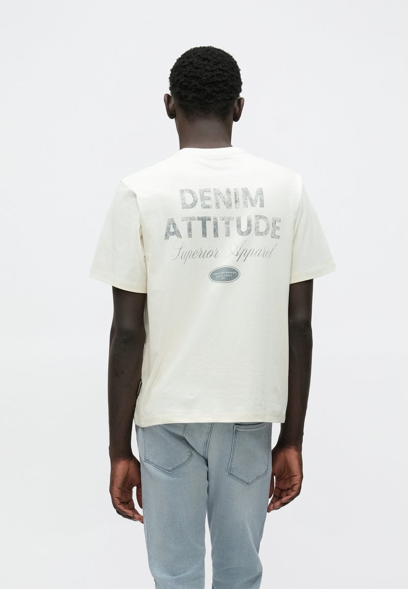 Μπλουζάκι από βαμβάκι σε κρεμ απόχρωση με γραφικό τύπωμα στην πλάτη που γράφει "DENIM ATTITUDE". Διαθέτει κοντά μανίκια και άνετη εφαρμογή.