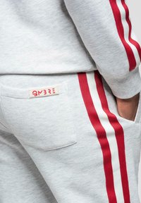 Lähikuva harmaista collegehousuista ja -paidasta, joissa on punaiset ja valkoiset sivuraidat, käsi taskussa.