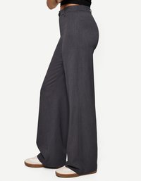 Wijduitlopende donkergrijze broek gemaakt van textuurstof, met een knoopsluiting en een gladde tailleband, gecombineerd met lichte sneakers.