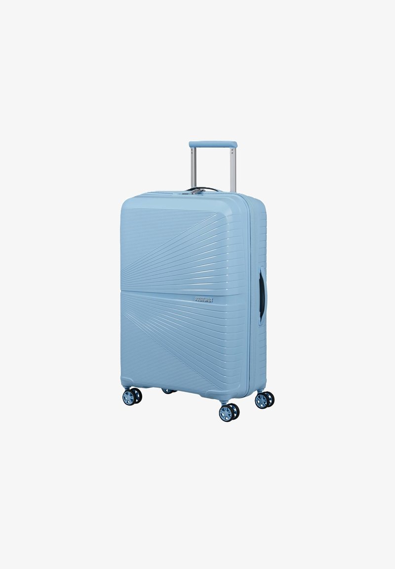 Valise rigide bleu clair avec quatre roues doubles pivotantes, lignes diagonales texturées, poignée télescopique et poignée latérale.