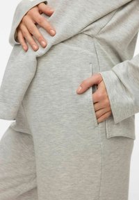 Gaiši pelēks mājas apģērbu komplekts no mīksta, fakturēta auduma. Tam ir garas piedurknes un sānu kabata, brīvs siluets un minimālas šuves.